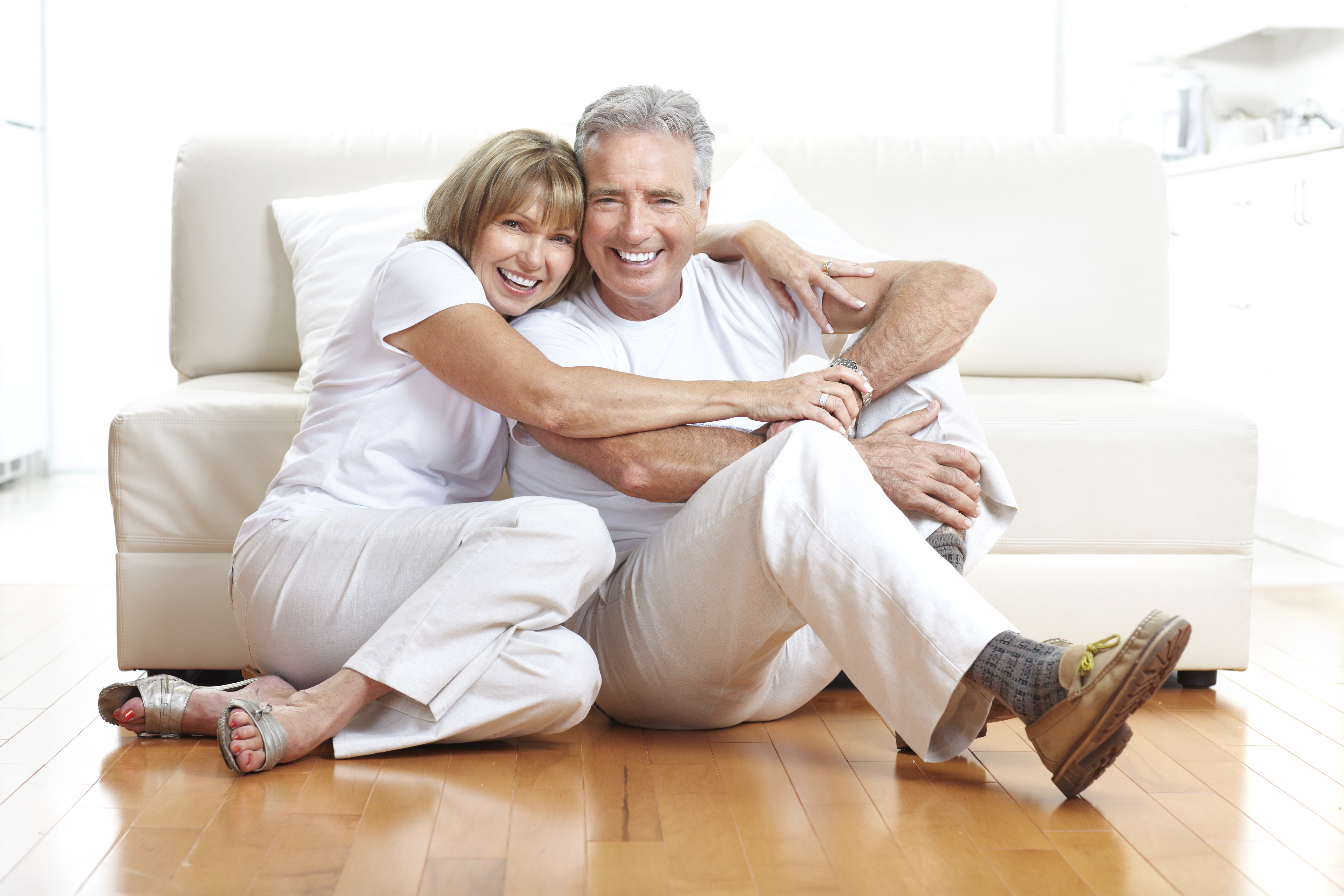 older couple sitting on hardwood floor hugging smiling happy partial dentures cosmetic dentistry